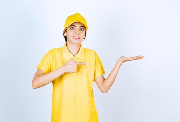 Leveringsvrouw in geel uniform staand en geopende handpalm.