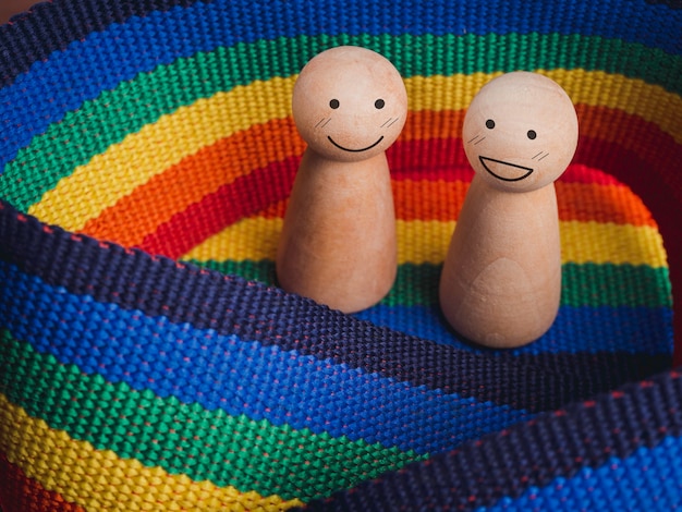 Lgbt-paarconcept. close-up twee houten figuren met rokvormen en blije glimlachgezichten die samen op de achtergrond van de regenboogvlag staan. lgbt-trotssymbool.