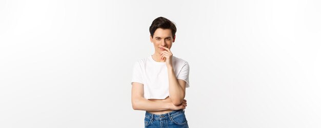 Lgbtq en trots concept Tevreden jonge homoseksuele man die denkt een idee te hebben en glimlacht terwijl hij naar de camera staart met een crop top witte achtergrond