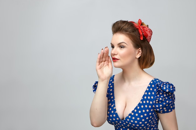 Lichaamstaal. foto van modieuze jonge europese vrouw in vintage jurk met lage nek uitgesneden hand houden aan haar mond alsof iemand belt of geheim in oor fluisteren, poseren in studio