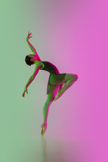 Licht. Jonge en gracieuze balletdanser die op roze-groene muur met gradiënt in neon wordt geïsoleerd. Kunst, beweging, actie, flexibiliteit, inspiratieconcept. Flexibele ballerina, gewichtloze sprongen.