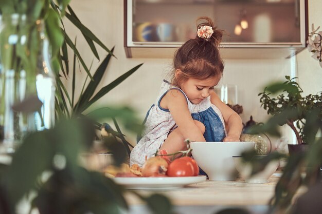 Lief klein schattig meisje leert een maaltijd te koken in de keuken terwijl ze op een aanrecht zit.