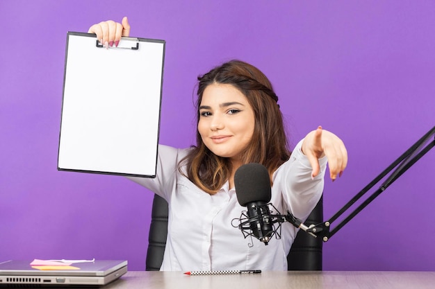 Lief meisje met notitieboekje en wijs met de vinger naar de camera mooi meisje zit achter bureau op paarse achtergrond foto van hoge kwaliteit