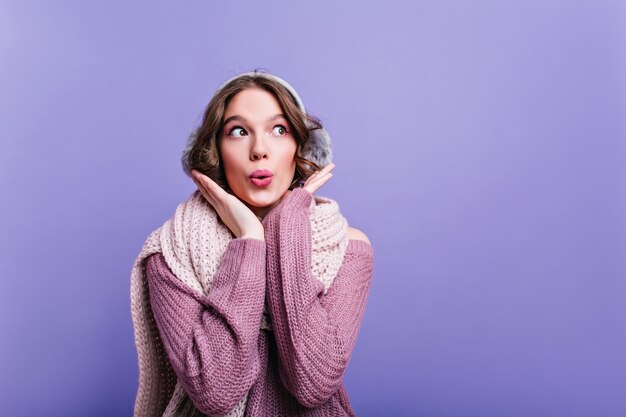 Lief meisje met zachte gebreide sjaal wegkijken met glimlach. Close-up indoor portret van mooie vrouw in warme paarse trui.