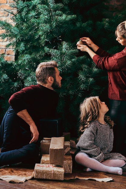 Liefde, familie, kerst. Aantrekkelijke familie siert de kerstboom, omringd door geschenken thuis.