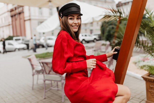 Liefdesdame in heldere Russische rode jurk dansen. Straatfoto van jonge sluikharige vrouwelijk model