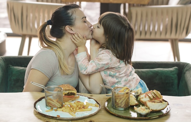 Liefdevolle familie. moeder met schattige dochter fastfood eten in een café, familie en voeding concept