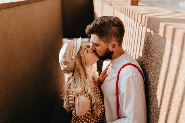 Liefhebbers kussen op straat tegen de achtergrond van betonnen muren. Jongen en vriendin met stijlvolle outfits poseren.