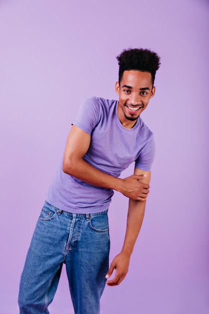 Lieve man lachen in spijkerbroek poseren. Binnenfoto van Afrikaans mannelijk model met trendy kapsel status.