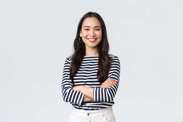 Lifestyle, beauty en mode, mensen emoties concept. Jonge Aziatische vrouwelijke officemanager, CEO met een tevreden uitdrukking op een witte achtergrond, glimlachend met gekruiste armen over de borst.