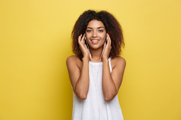 Lifestyle concept - portret van mooie afrikaanse amerikaanse vrouw blij muziek aan de mobiele telefoon te luisteren. gele pastel studio achtergrond. ruimte kopiëren.