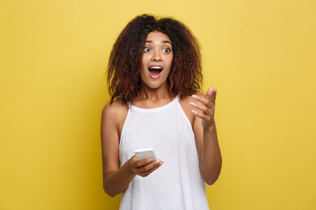 Lifestyle Concept - Portret van mooie Afrikaanse Amerikaanse vrouw schokkend met iets op de mobiele telefoon. Gele pastel studio achtergrond. Ruimte kopiëren.