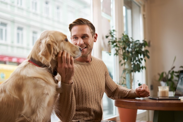 Lifestyle foto van een jonge knappe ondernemer die in een café aan een laptop werkt terwijl zijn hond zit