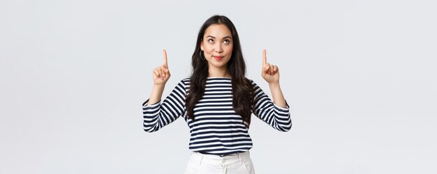 Lifestyle mensen emoties concept Opgewonden knap Aziatisch meisje glimlachend tevreden zoals gevonden uitstekend product wijzende vingers naar advertentie en tevreden kijken promo aanbevelen