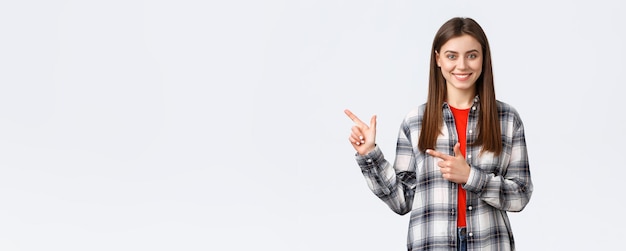 Lifestyle verschillende emoties vrijetijdsactiviteiten concept aangenaam lachend brunette meisje in geruit overhemd wijzende vingers naar links tonen weg naar promo aanbevelen klik op link of koop product
