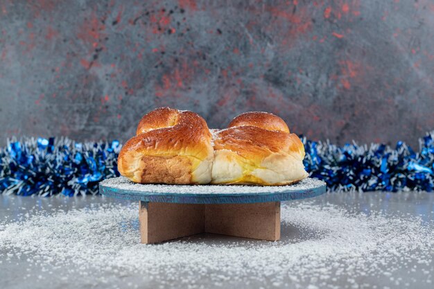 Lijn van klatergoud achter een zoet broodje op een standaard op marmeren tafel.