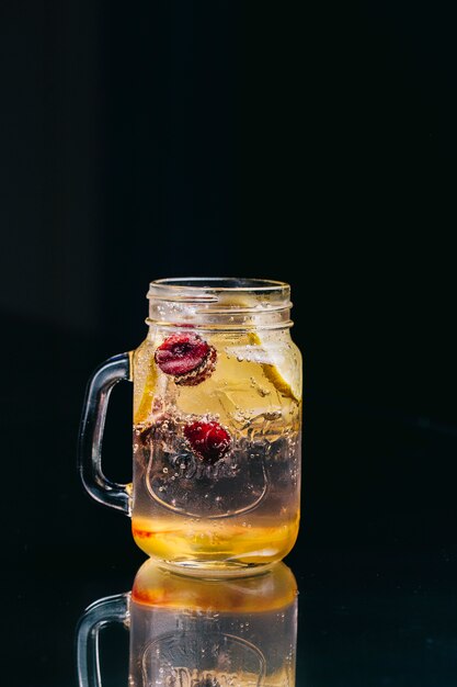 Limonade met bessen in glazen pot in een zwarte ruimte.