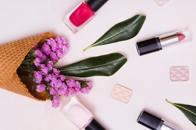 Limonium en blad in de wafelkegel; nagellakfles; lippenstift en oogschaduw op roze achtergrond