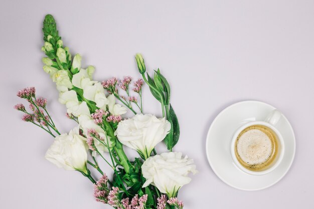 Limonium; eustoma en leeuwebekken bloemboeket dichtbij de koffiekop op witte achtergrond