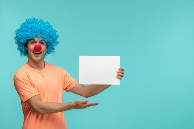 Links van het middenaanzicht april dwazen dag kerel clown blij wijzende vinger met papier blauw haar opgewonden grappige rode neus