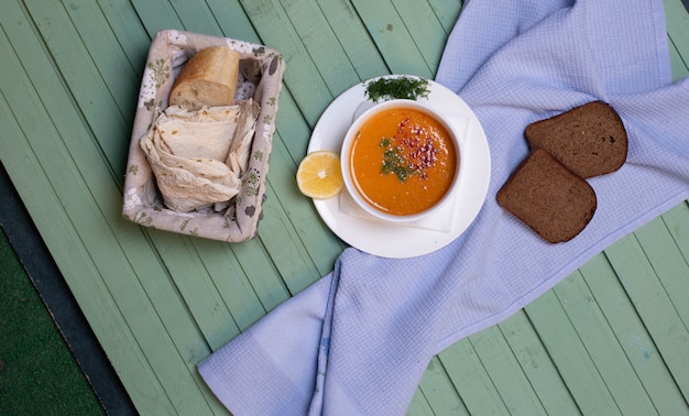 Linzensoep geserveerd met citroen en brood segmenten op een blauwe tafel