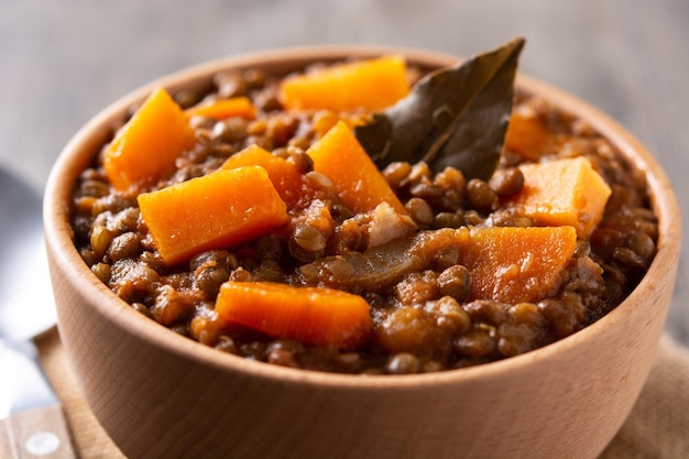 Linzenstoofpot ragout met pompoen en wortel in kom op houten tafel