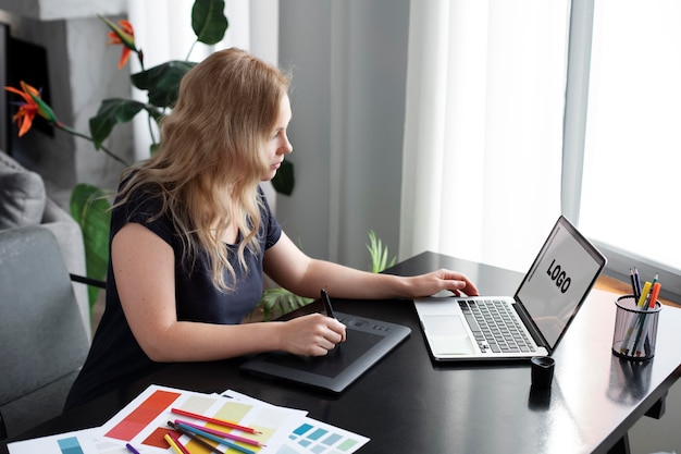 Logo-ontwerper werkt aan haar tablet die is aangesloten op een laptop