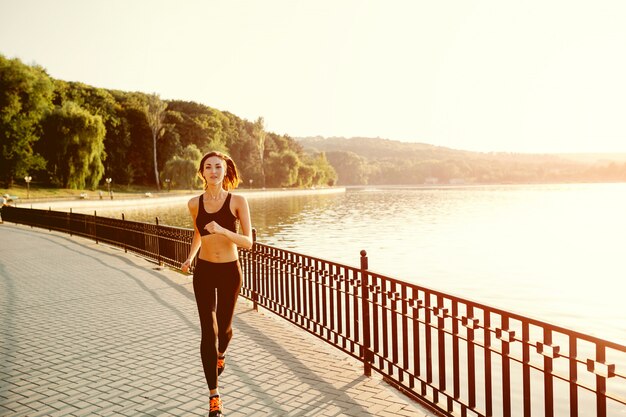 Lopende vrouw. Runner joggen in zonnig helder licht. Vrouwelijke fitness model training buiten in het park