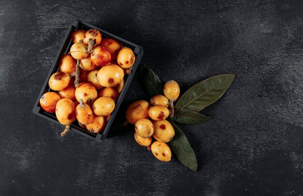 Loquats met bladeren in een zwarte doos op donkere gestructureerde achtergrond, bovenaanzicht.