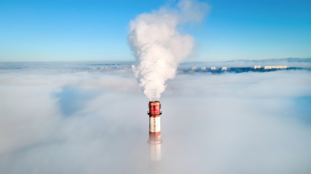 Luchtfoto drone-weergave van de buis van het thermische station zichtbaar boven de wolken met rook die naar buiten komt.