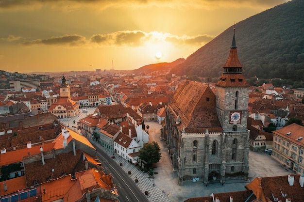 Gratis foto luchtfoto drone-weergave van de zwarte kerk in het oude centrum van brasov bij zonsondergang roemenië oude woongebouwen eromheen heuvels met groen