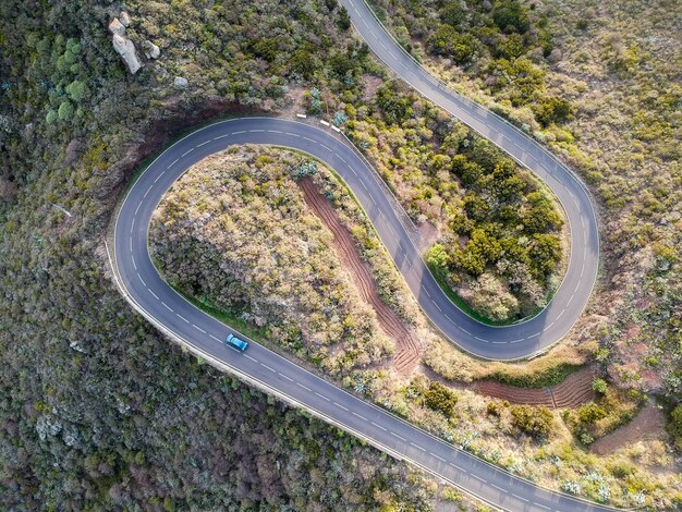 Luchtfoto van een auto die door een spiraalvormige weg rijdt, omringd door bomen op het platteland