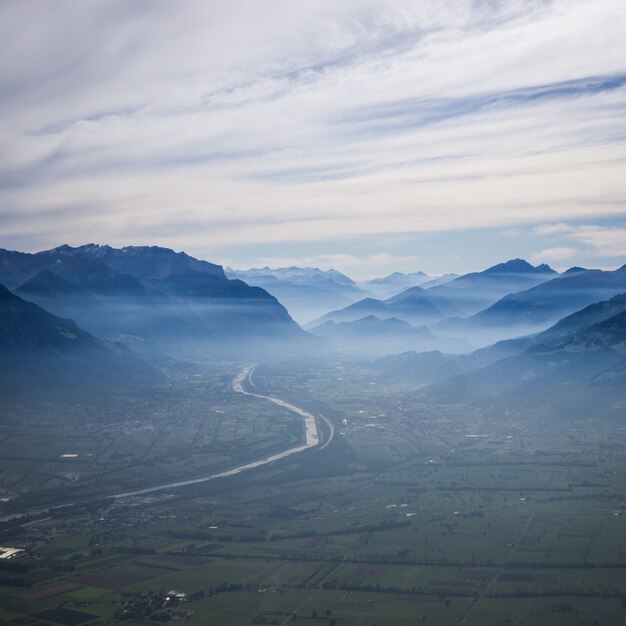 Luchtfoto van een bochtige weg naar de bergen in de mist onder een bewolkte hemel