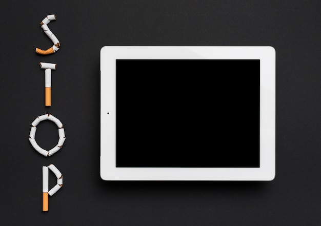 Gratis foto luchtmening van digitale die tablet met eindewoord van sigaret tegen zwarte achtergrond wordt gemaakt