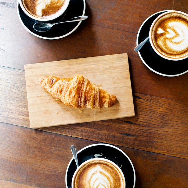 Luchtmening van koffiekoppen en croissant op houten lijst