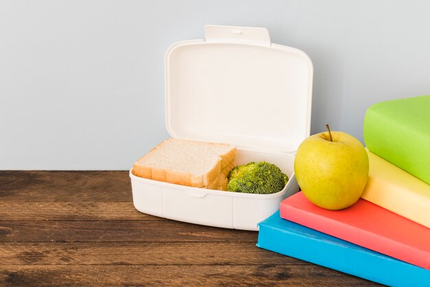 Lunchbox in de buurt van appel en kleurrijke boeken