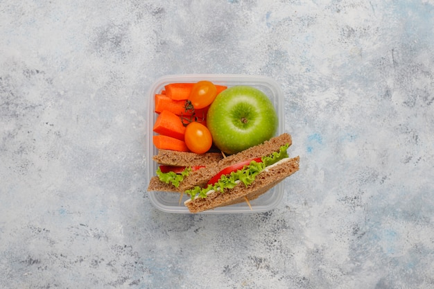 Lunchbox met sandwich, groenten, fruit op wit.