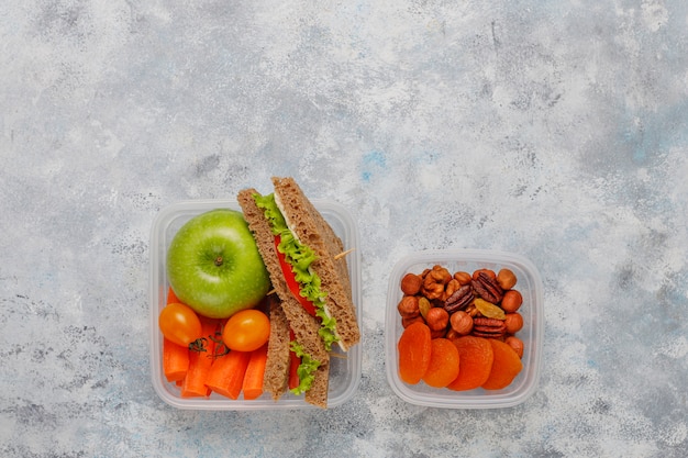 Lunchbox met sandwich, groenten, fruit op wit.