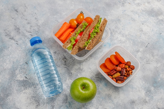 Lunchbox met sandwich, groenten, fruit op wit.