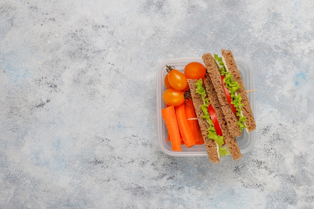 Lunchbox met sandwich, groenten, fruit op wit.