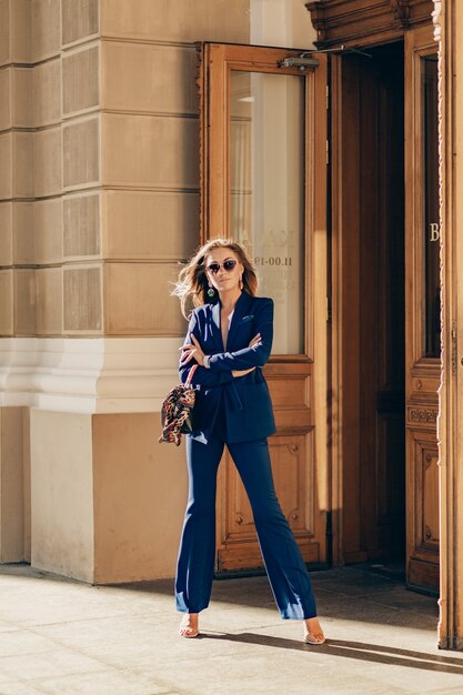 Luxe rijke vrouw gekleed in een elegante stijlvolle blauwe pak wandelen in de stad op zonnige herfstdag met portemonnee