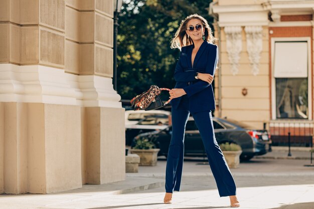 Luxe rijke vrouw gekleed in een elegante stijlvolle blauwe pak wandelen in de stad op zonnige zomerdag met portemonnee