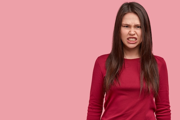 Maak me niet boos. Depressieve, donkerharige jonge vrouw klemt zijn tanden met ergernis, fronst gezicht van ontevredenheid, drukt afkeer uit