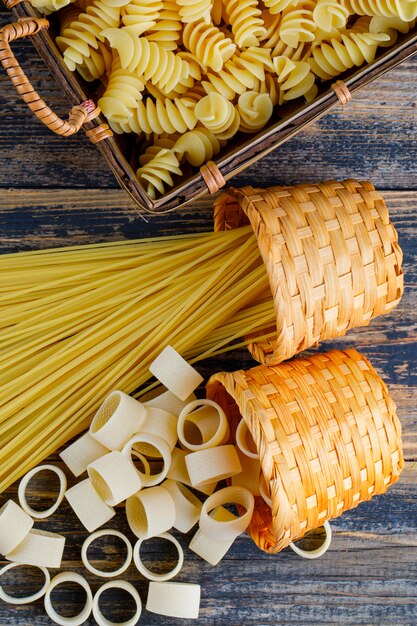 Macaroni in een emmer en dienblad met pasta en spaghetti bovenaanzicht op een donkere houten achtergrond