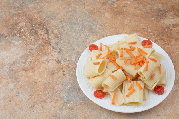 Macaroni met wortel en tomatenkers op witte plaat.