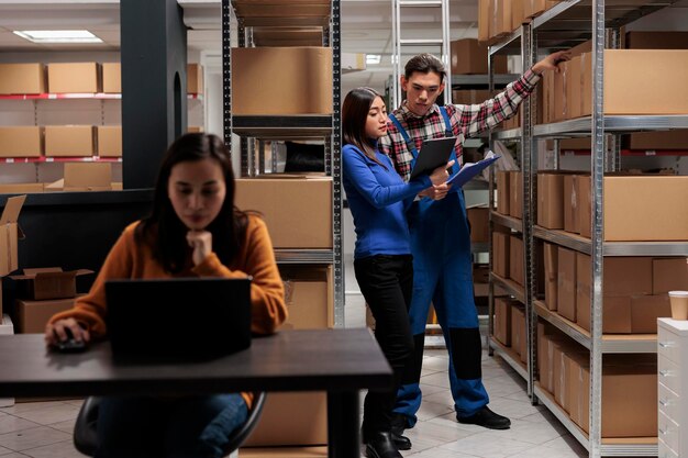 Magazijnmedewerker en logistiek manager die producten controleren in de opslagruimte. Medewerkers van het magazijn beheren de kwaliteitscontrole van goederenpakketten terwijl ze gegevens analyseren op het klembord en op een digitale tablet