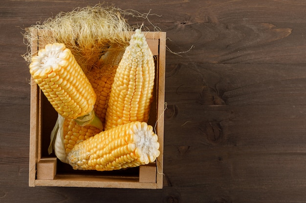 Gratis foto maïskolven in een houten doos met plakken hoogste mening over een donkere houten lijst