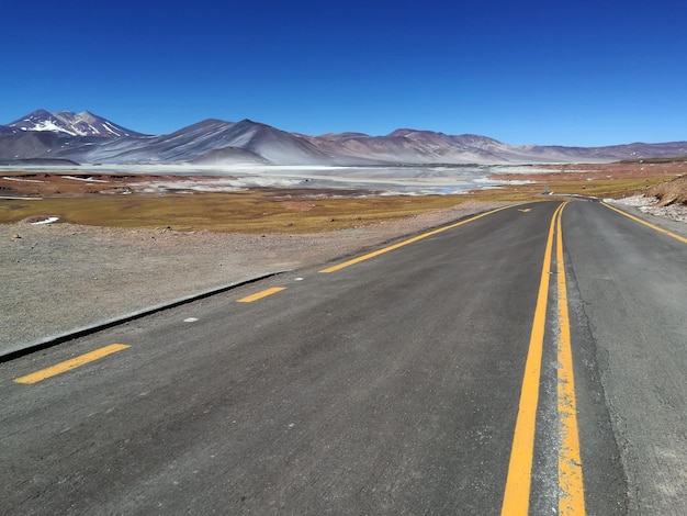 Majestueuze scène van een verharde rechte snelweg die op een zonnige dag door een met sneeuw bedekte bergketen gaat