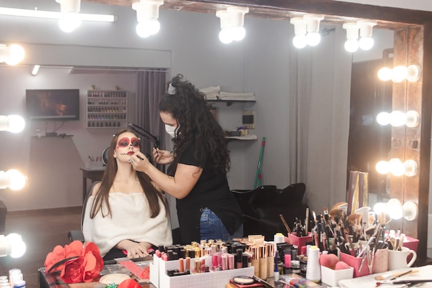 Make-up artiest afwerking details van een dia de los muertos make-up voor een mooi meisje in de schoonheidssalon.