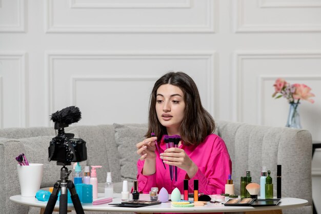 Gratis foto make-up blogger schattige mooie mooie jonge dame die video op camera opneemt met veel borstels